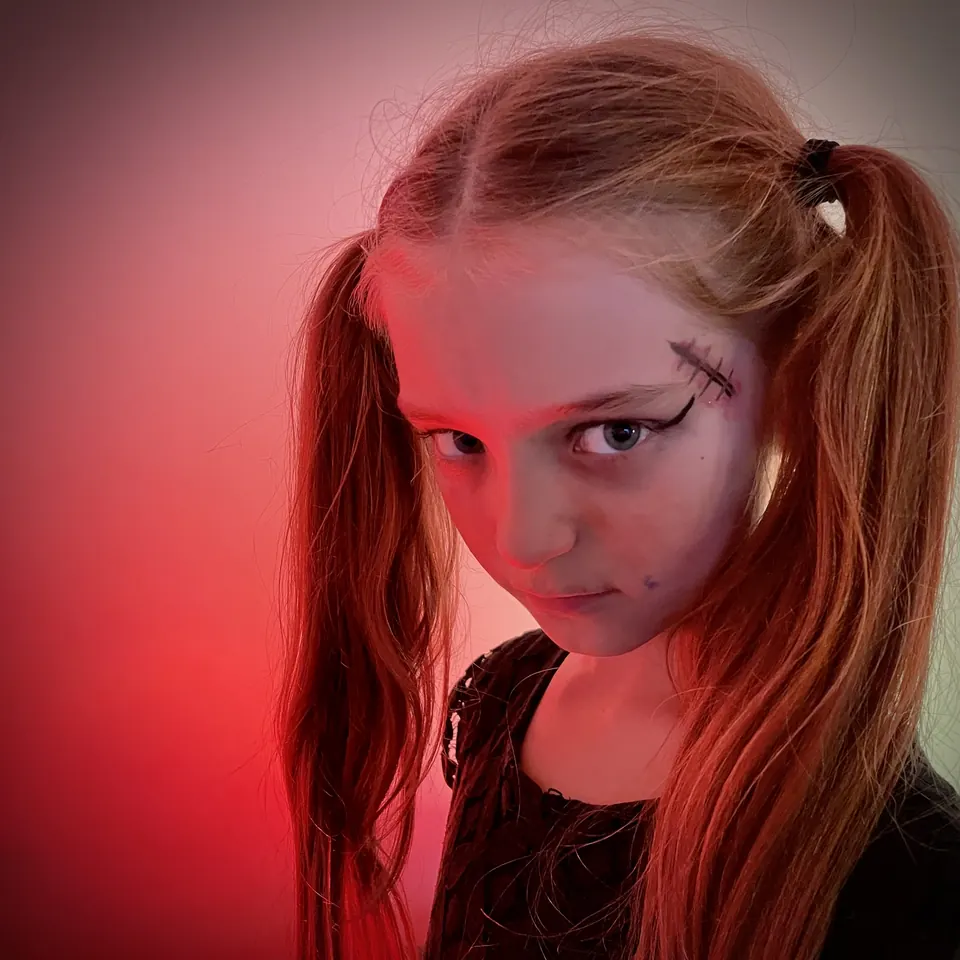 Manon Maindivide portrait in red light with pigtails and dark special effects makeup across her face