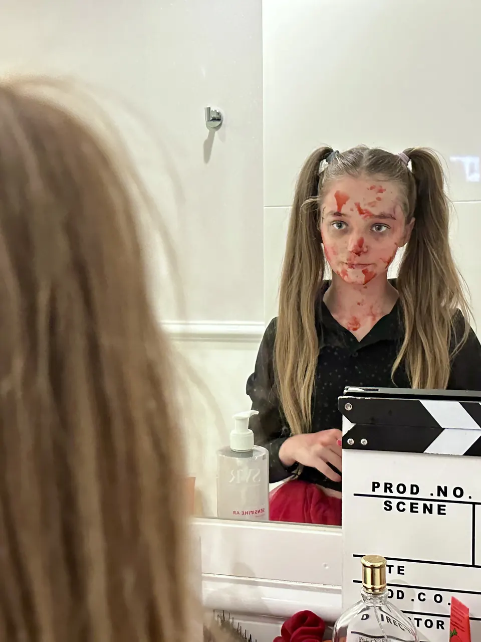 Manon Maindivide behind the scenes with fake blood makeup and pigtails, a film clapperboard beside her