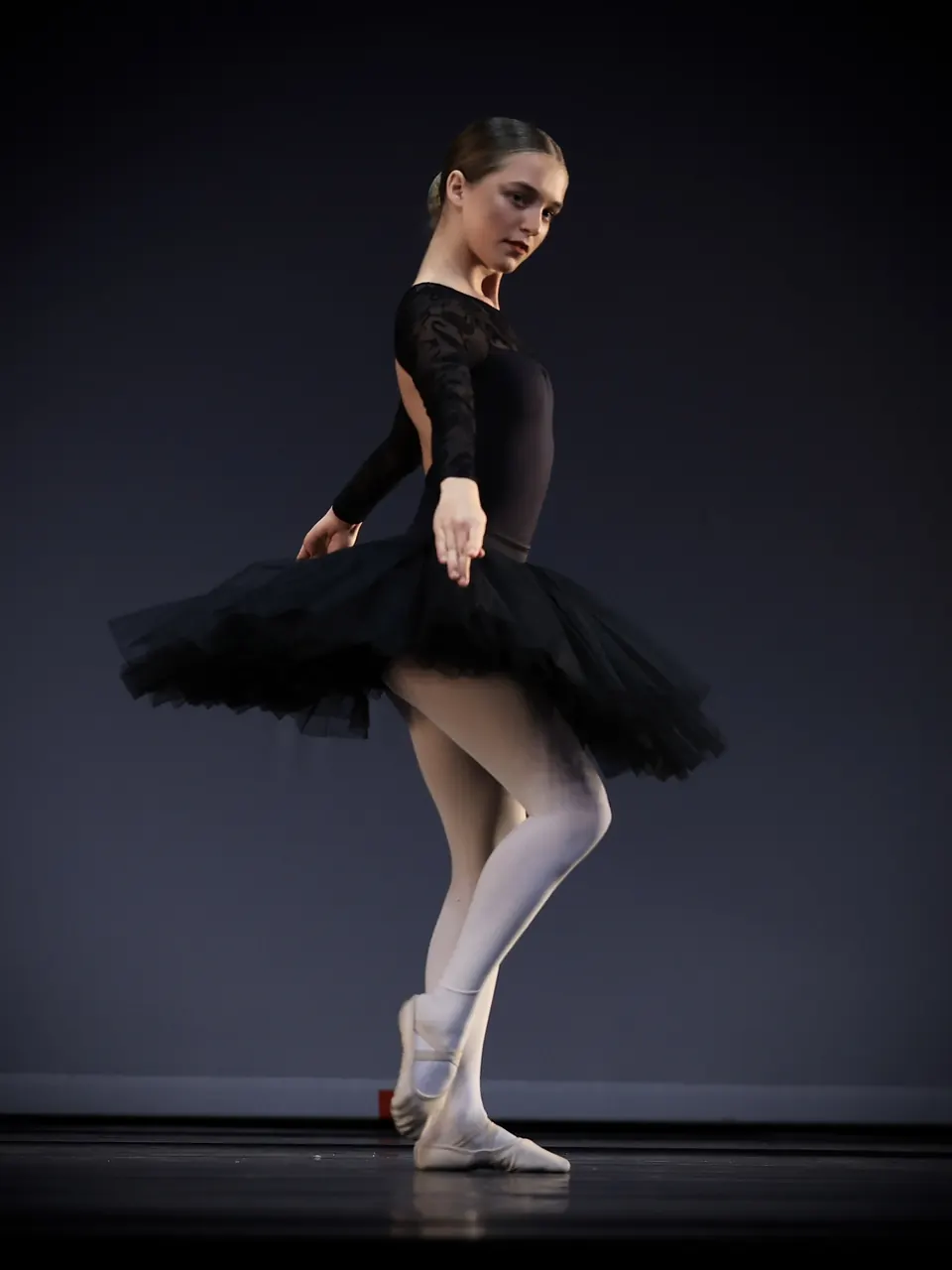 Manon Maindivide dance performance in a black tutu and lace top, poised on a dark stage