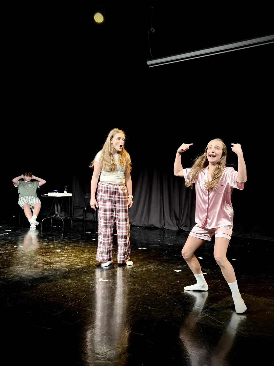 Manon Maindivide on stage in pink pyjamas with another performer in plaid, dancing on a black floor