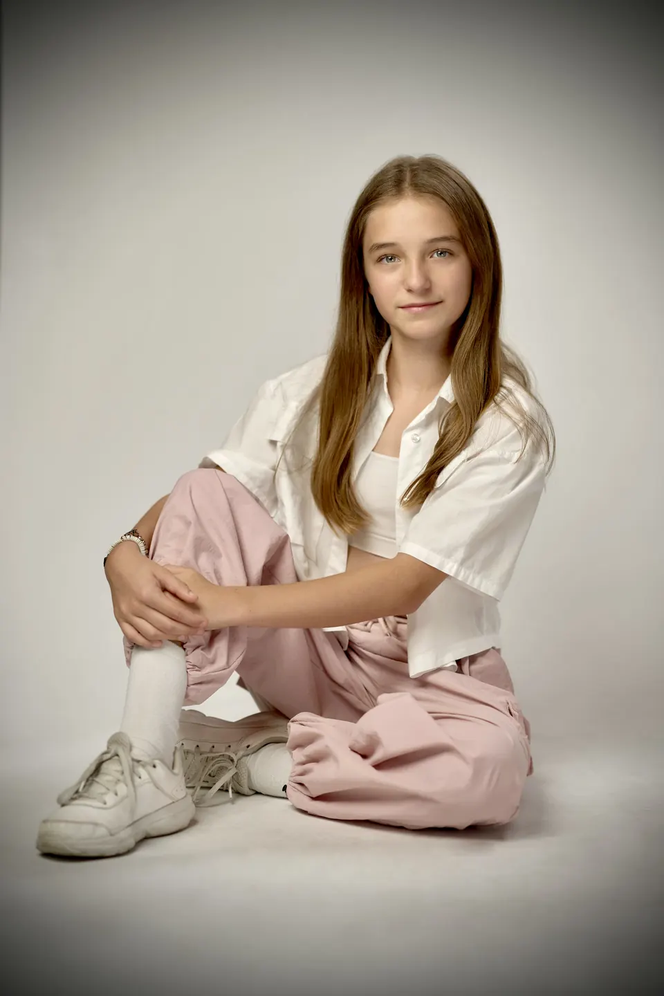 Manon Maindivide photo shoot seated on the studio floor in a white shirt and pink trousers