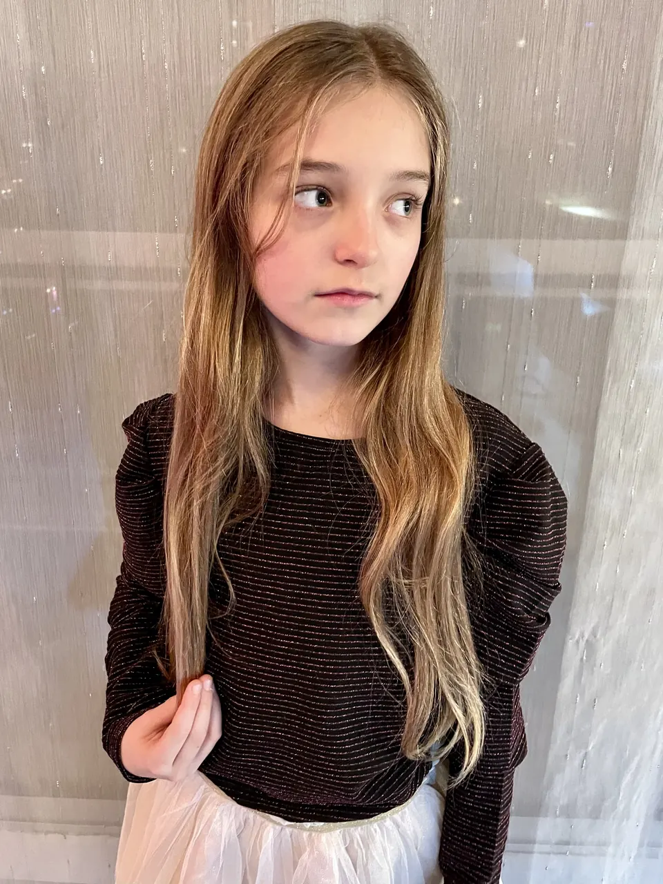 Manon Maindivide portrait in a dark knit top, glancing sideways in front of a sheer white curtain