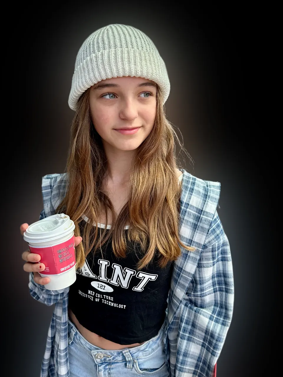 Manon Maindivide photo shoot in a grey beanie and plaid shirt, holding a takeaway cup, dark background
