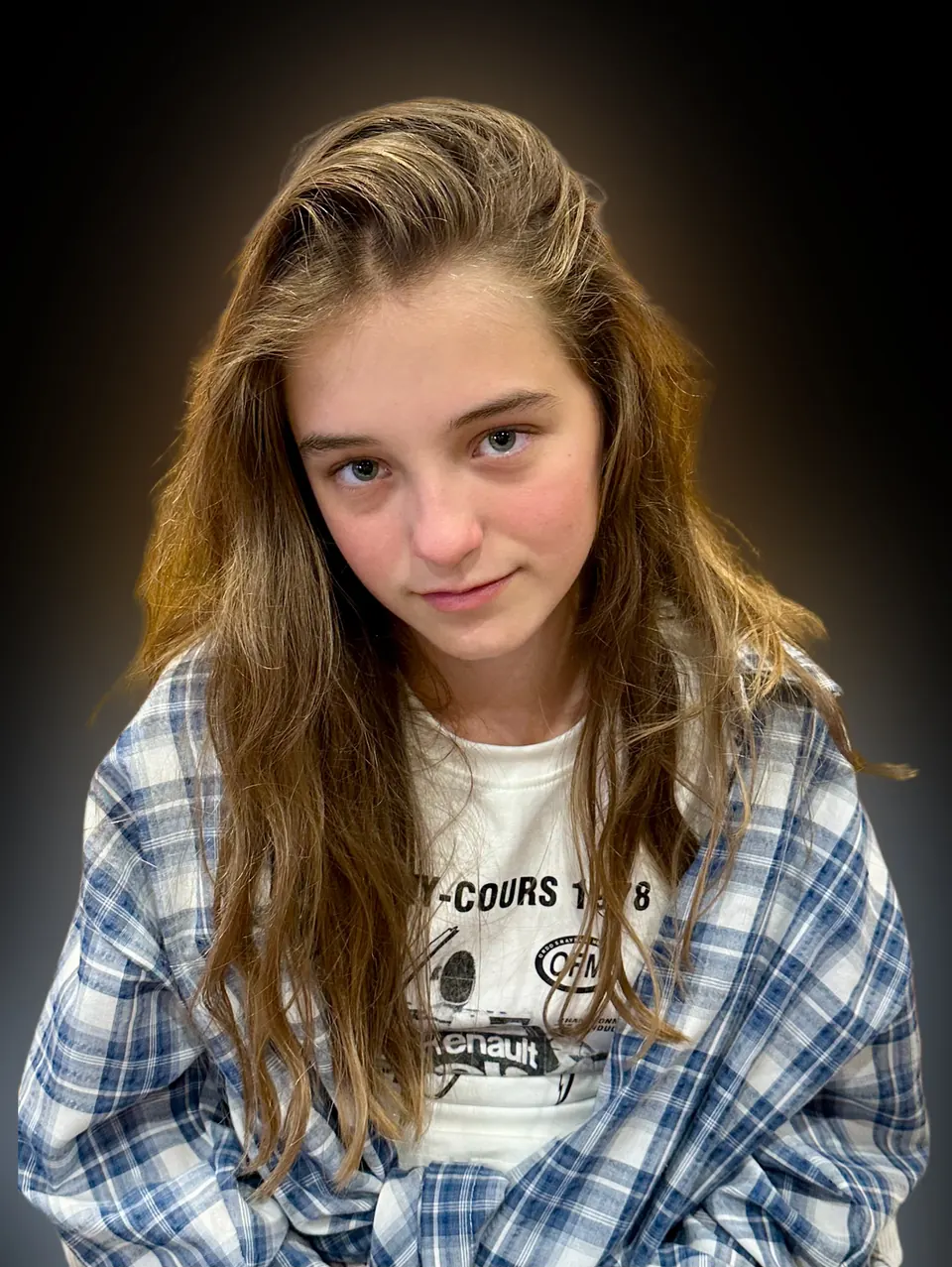 Manon Maindivide headshot in a blue plaid shirt and white tee, warm light on a dark backdrop
