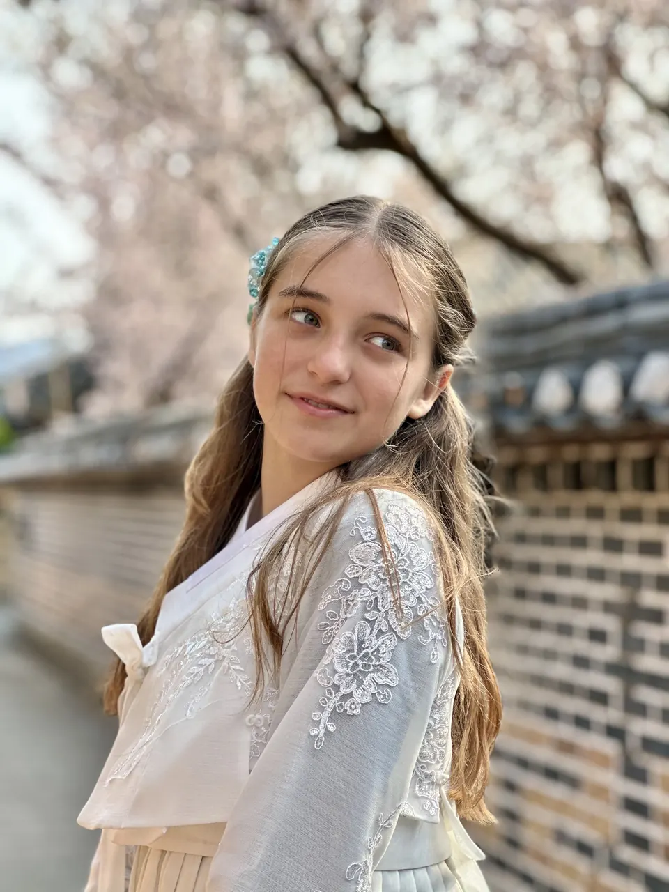 Manon Maindivide portrait in a white embroidered outfit, looking aside near a stone wall