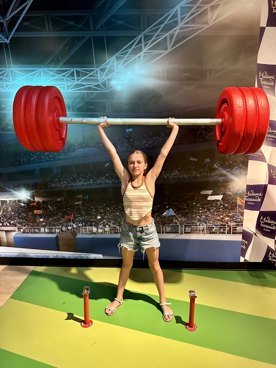 Manon Maindivide casual photo posing under a giant red barbell prop with an arena backdrop