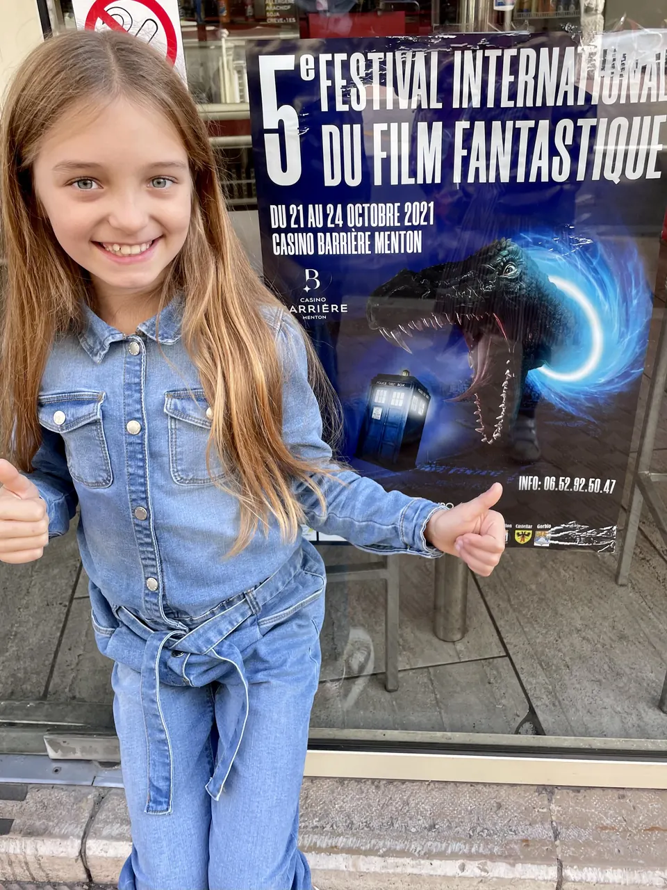 Manon Maindivide in a denim jumpsuit giving thumbs up beside a film festival poster