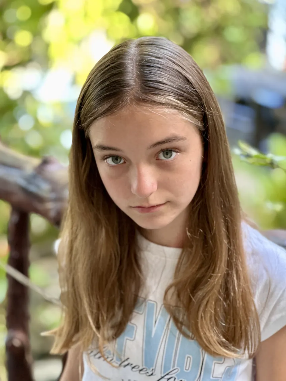 Manon Maindivide close-up portrait in a white t-shirt, steady gaze with green leaves behind