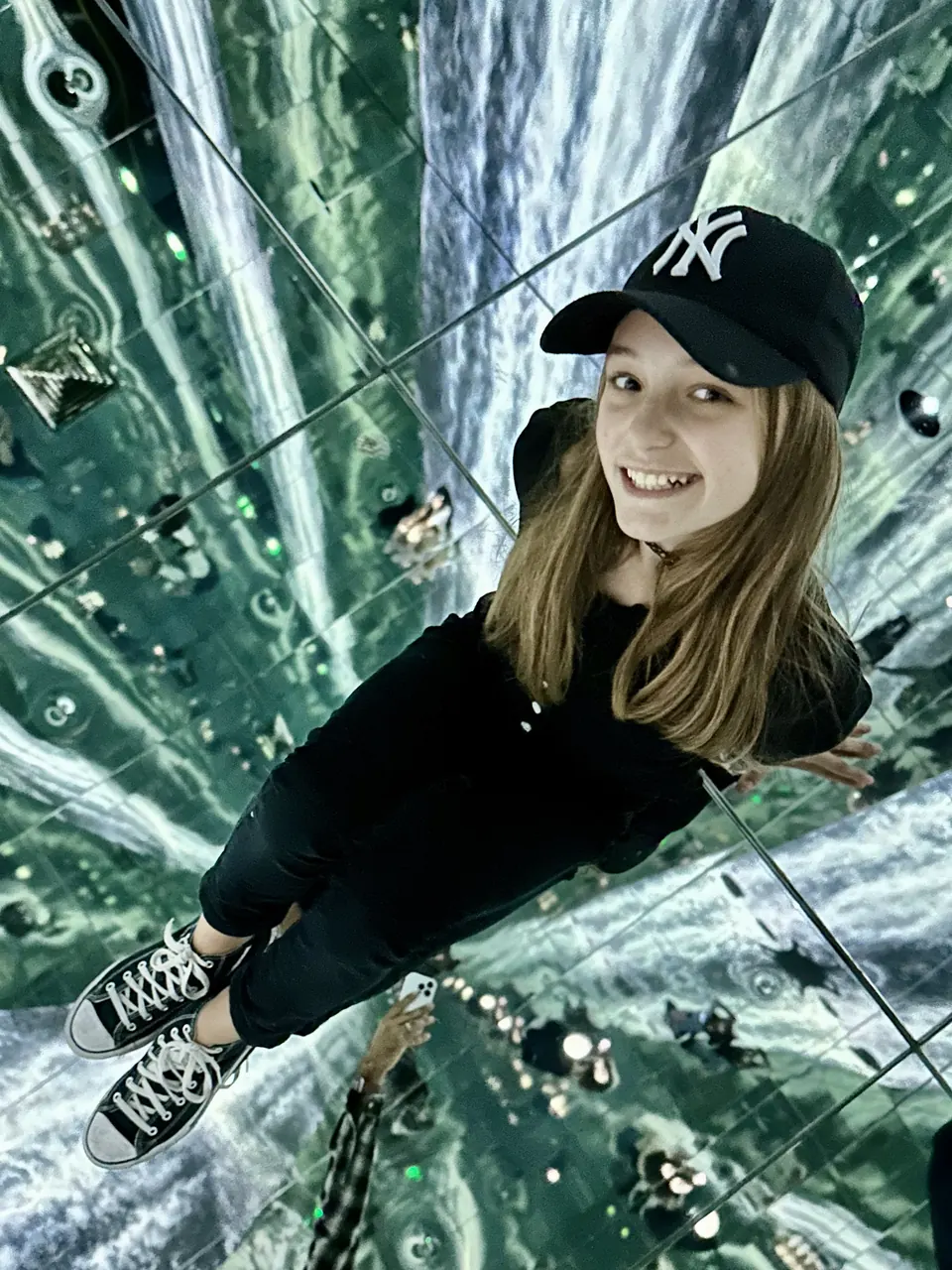 Manon Maindivide casual photo in a black cap, posing on a mirrored floor that reflects the ceiling