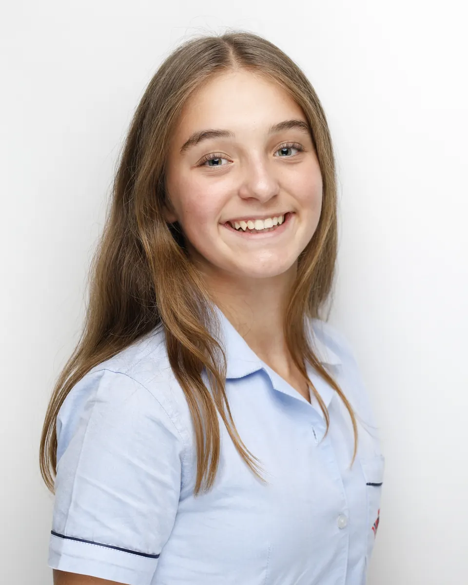 Manon Maindivide headshot in a light blue polo shirt, wide smile on a plain white backdrop
