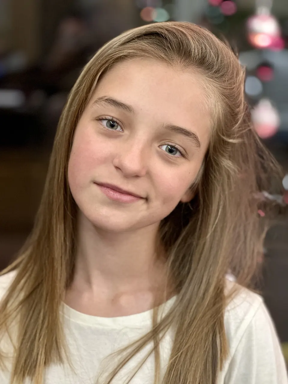 Manon Maindivide headshot with long hair and a cream top, soft festive lights behind her