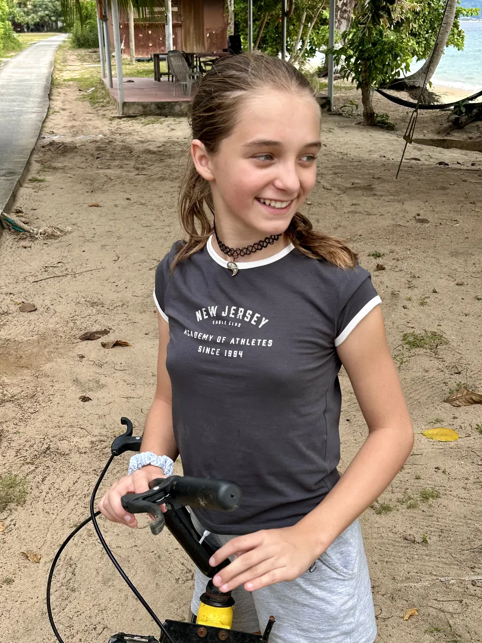 Manon Maindivide casual photo on a sandy path with a bicycle, smiling in a grey T-shirt