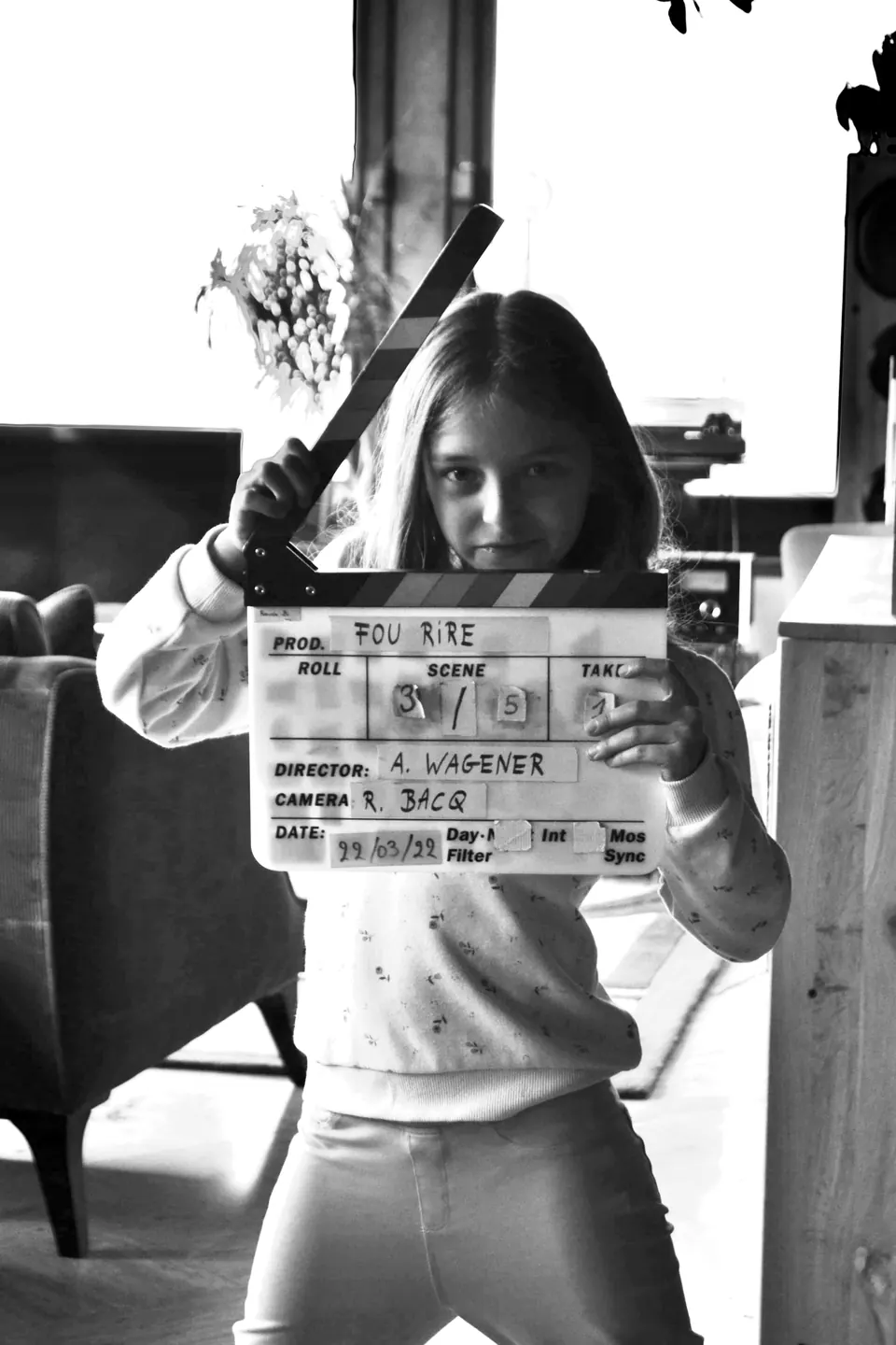 Manon Maindivide behind the scenes, holding up a film clapperboard in black and white