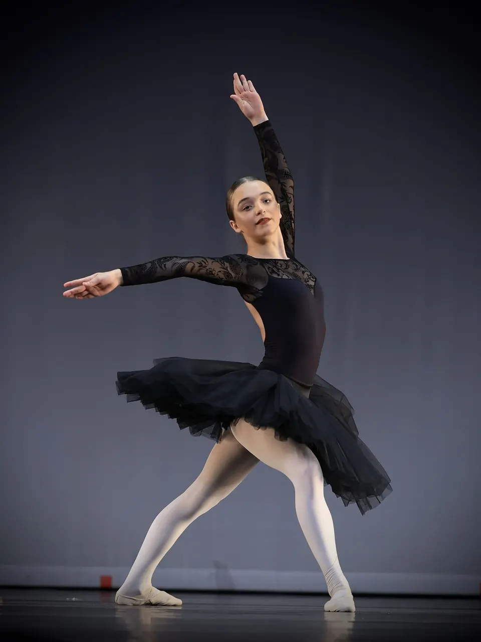 Manon Maindivide dance performance in a black tutu, arm raised gracefully on a grey stage