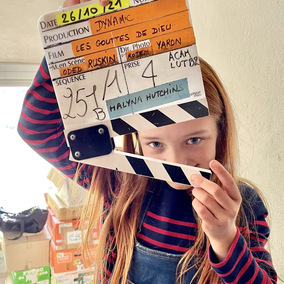 Manon Maindivide on set holding a film clapperboard in front of her face, striped sweater