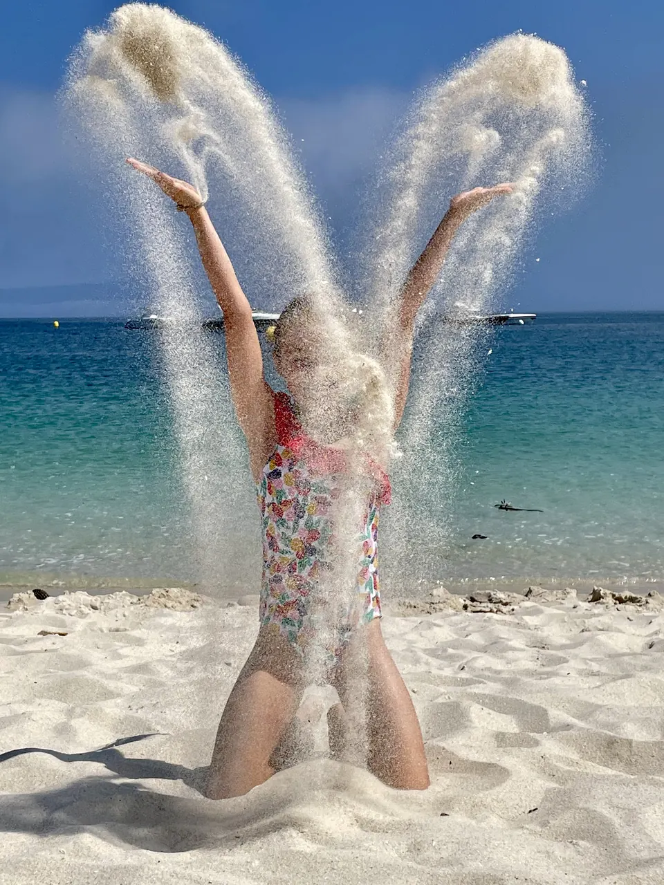 Manon Maindivide photo shoot on a beach, kneeling in the sand as she tosses sand into the air